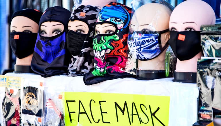 A street vendor has a table set up with mannequin heads wearing face masks