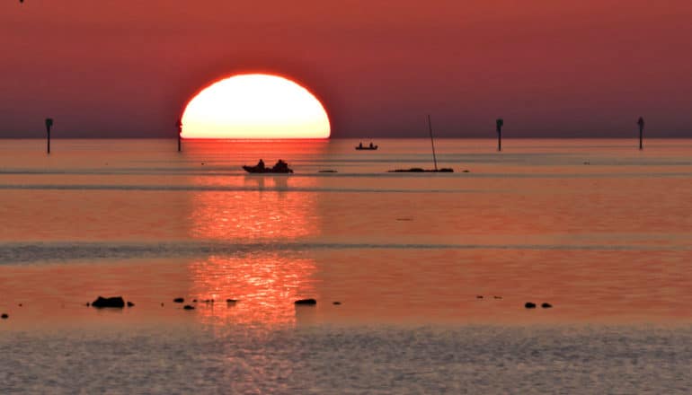 sunset over water with fishing boat in silhouette