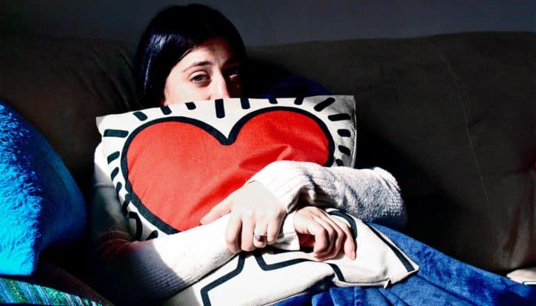 A young woman hugs a pillow with a heart on it while sitting on the couch