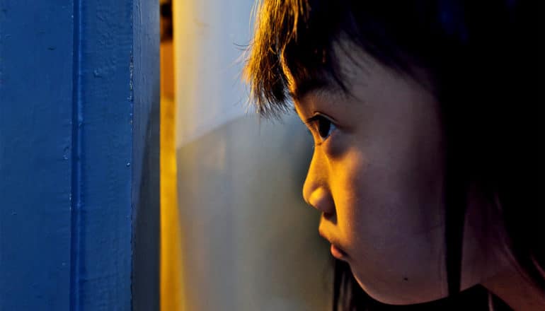 A young girl looks through a slightly-opened door