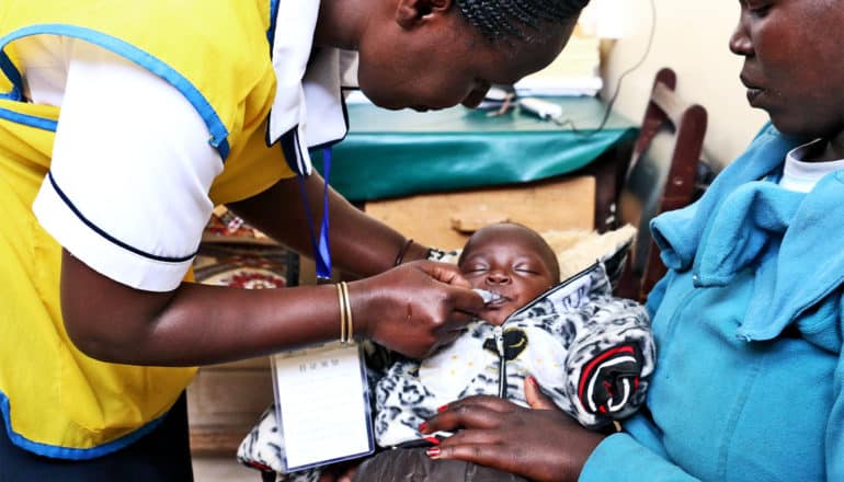 A baby gets a oral vaccine from a health worker in a yellow vest