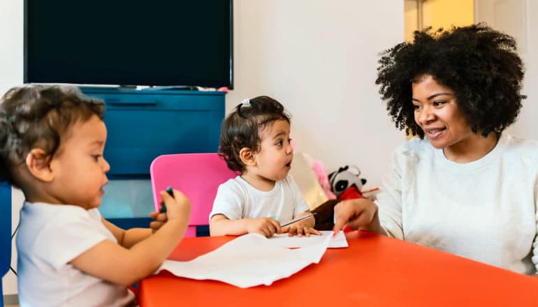 parent and twin toddlers at table with paper and pens