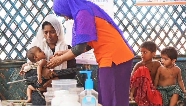 person examines baby held by mother; toddlers look on