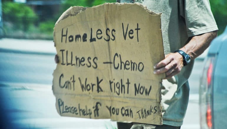 hand holds sign that says "homeless vet illness - chemo can't work right now please help if you can thanks"