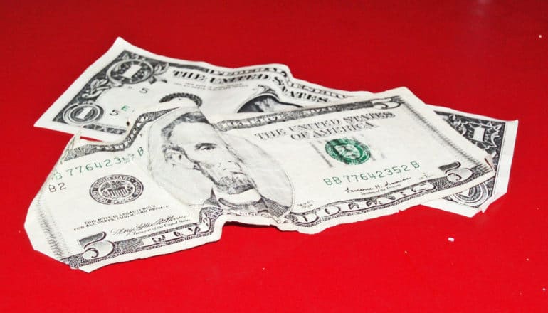 crumpled $5 and $1 bills on red surface