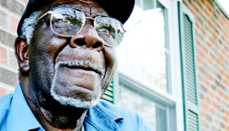 A man on his porch looks upwards while slightly smiling