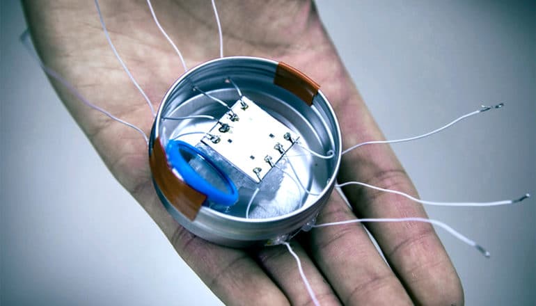 The small origami microbot sits in the hand of a researcher with wires coming out of a central hub