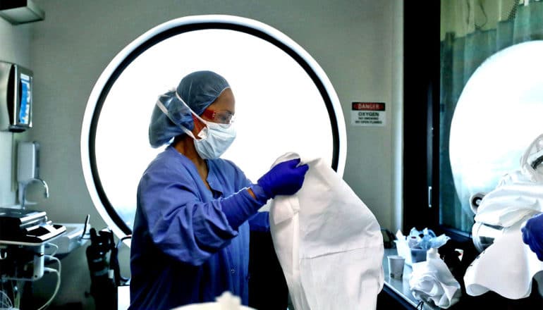 A nurse in full PPE cleans other gear in front of a circular window