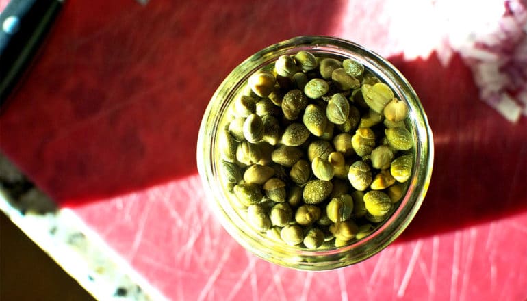 A jar of capers on a red cutting board