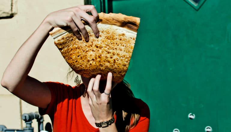 A woman eats a large slice of pizza that covers her face