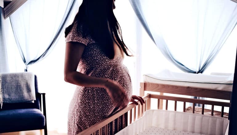 A pregnant woman looks down at a crib in a nursery