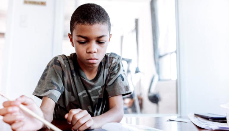 serious Black child with pencil at table