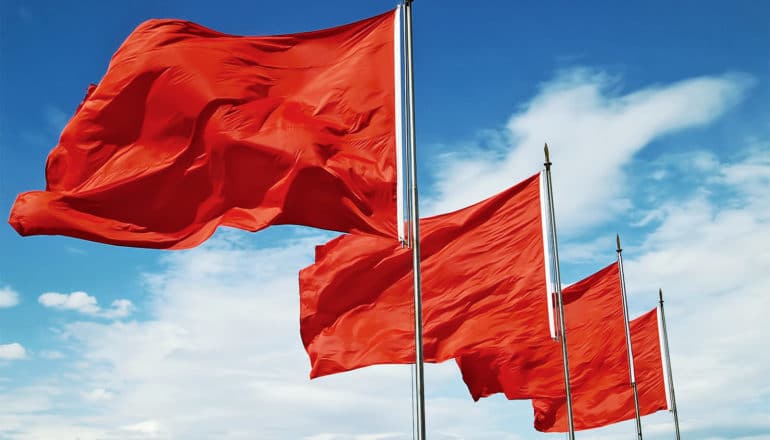 Red flags flap in the wind against a blue sky