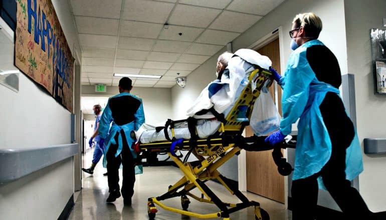 Health care workers roll a patient on a gurney through a hospital hallway