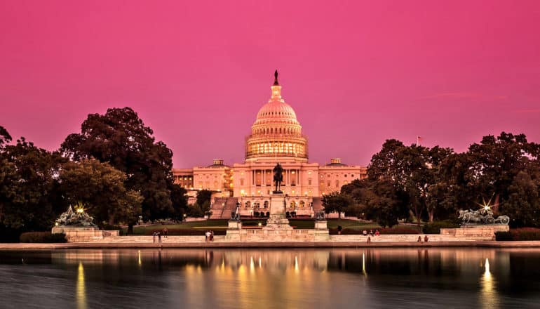 The US capitol building in Washington DC stands against a pink sky at sunset