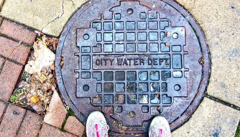 A person stands on a manhole cover that reads "City Water Dept."