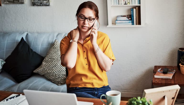 person holds neck while taking on phone at home desk