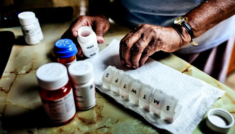 An older man sorts out his prescription medications with a pill container