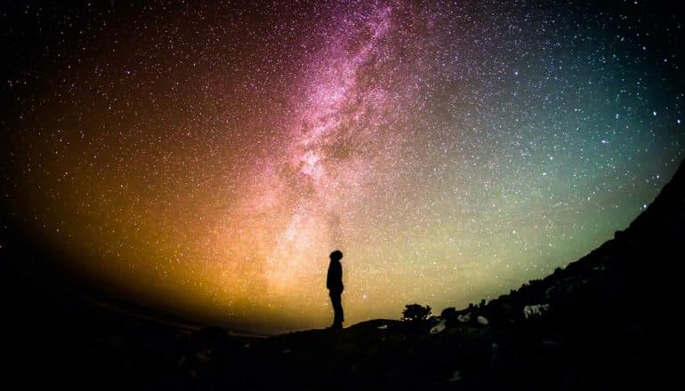 person in silhouette under colorful night sky