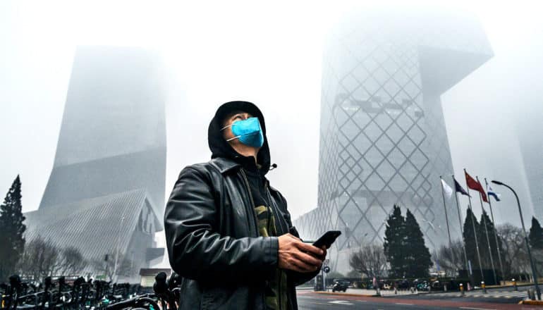 A man looks up at a polluted sky and obscured buildings with smog