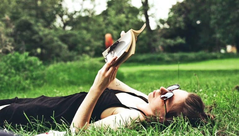 A woman lays on the grass reading a book