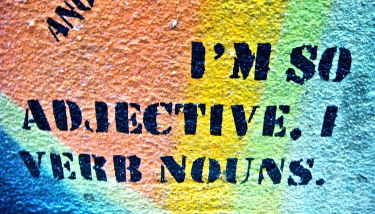 Words on a colorful wall read "I'm so adjective, I verb nouns."