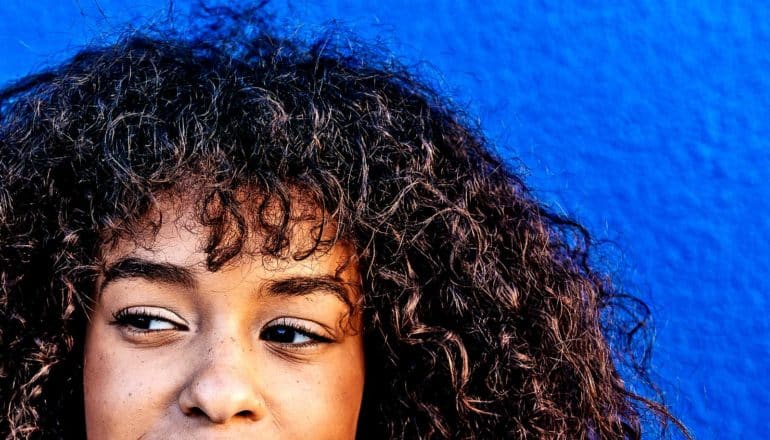 A young woman looks to her right while against a blue wall