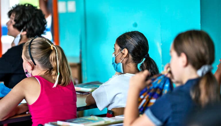 Young students sit in a classroom wearing face masks