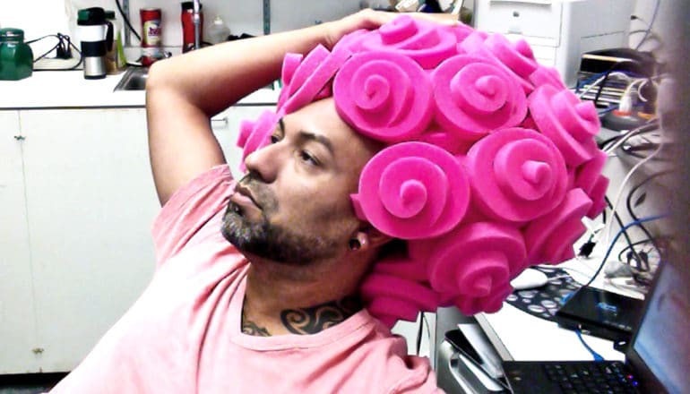 A man leans back in a chair with a large pink brain-shaped hat on his head