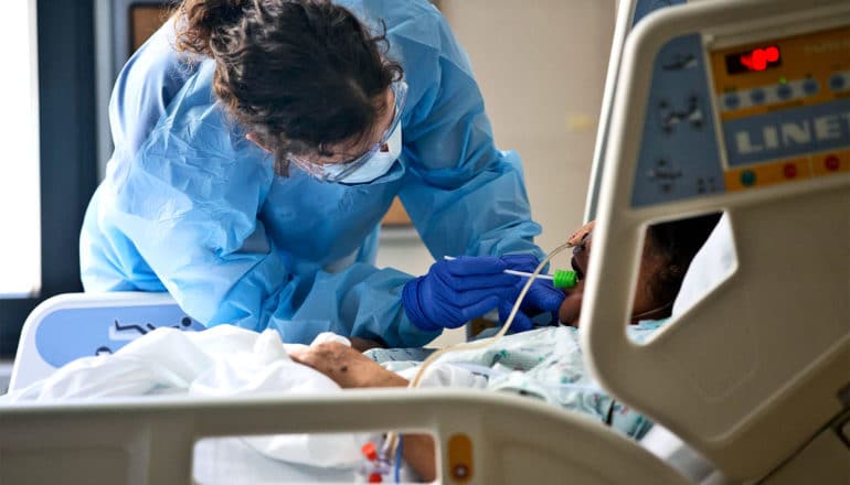 A hospital worker cleans a COVID-19 patient's mouth with a tool