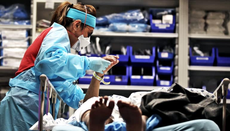 A health worker holds the hand of a patient with COVID-19