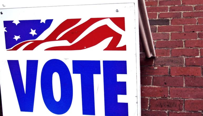 A sign has an American flag on it and reads, "VOTE" in blue letters