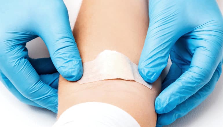 A doctor wearing blue gloves places a bandaid over over a blood draw on a young person's arm