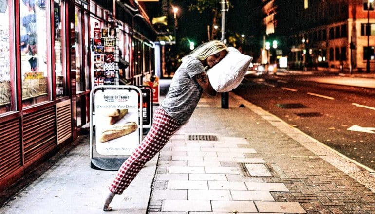 A woman leans on a floating pillow on a sitting street, almost levitating