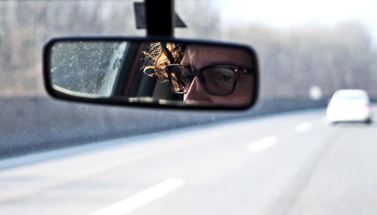 A man's eyes are visible in a rear view mirror