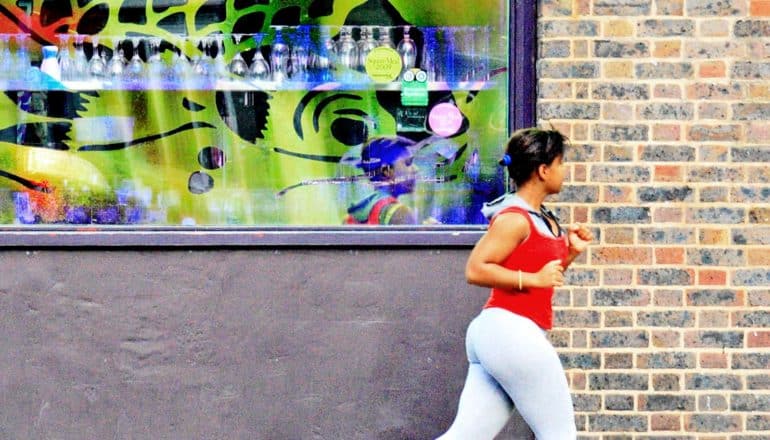 A woman jogs past a window with colorful bottles displayed