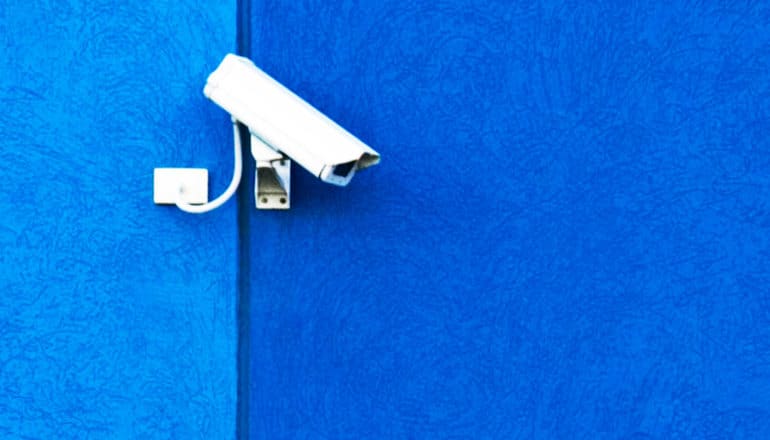 A cctv security camera looks down from high on a bright blue wall