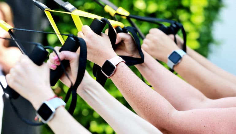 A group of people wearing fitness tracker watches pull on resistance bands, with just their arms visible