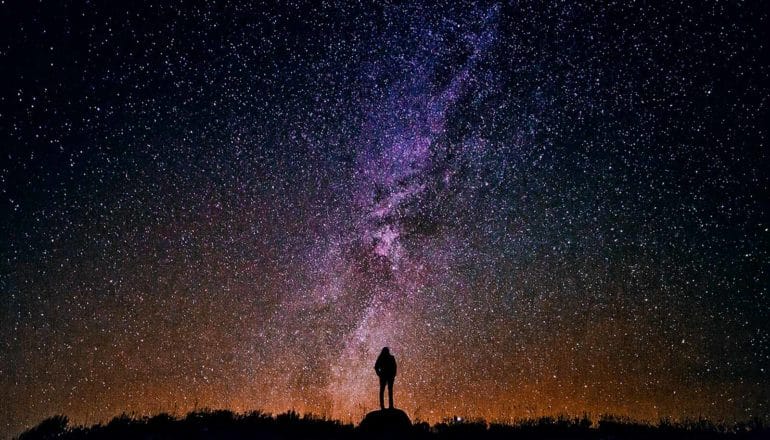 A person in silhouette looks up at a starry sky