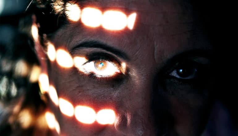 A woman's eye is covered in light as she sits in the dark