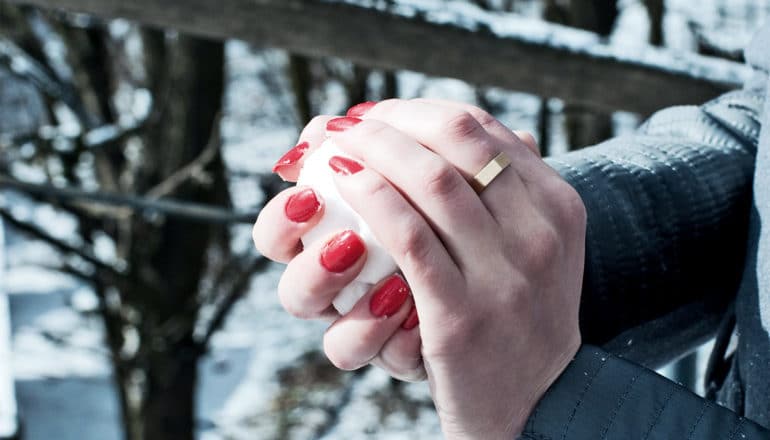 A woman with bright red nails packs a snowball in her hands