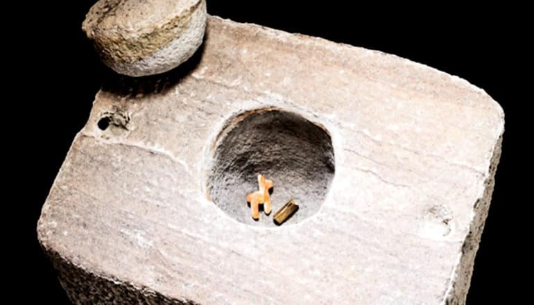 The tiny llama shell carving sits in the bottom of a carved hole in a large square rock that has a large stone lid sitting nearby