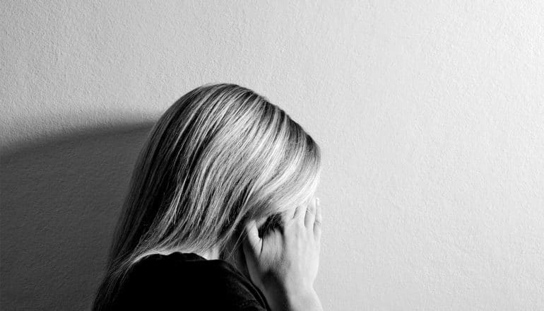 A woman puts her head in her hands against a white wall