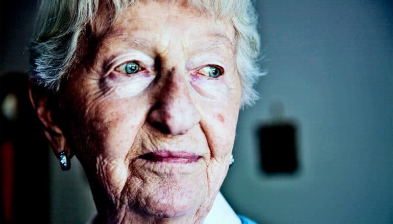 An older woman with a slight smile on her lips looks lost in thought