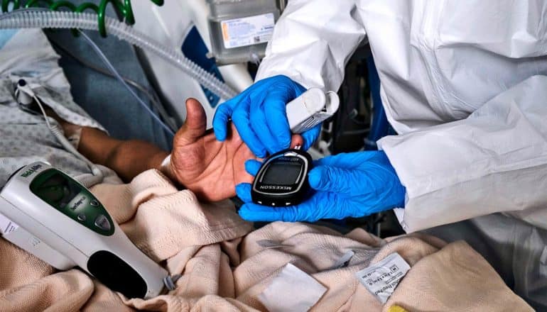 A health worker performs a blood sugar test on a patient in a hospital bed