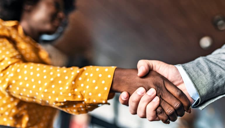 A women with natural hair in a yellow shirt shakes a man's hand during a job interview