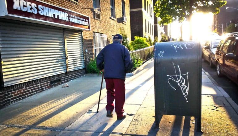 An older man walks down the city street with the sun setting ahead of him