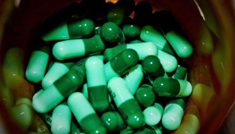 A bottle is filled with green pills