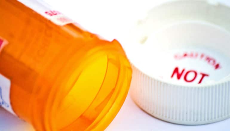 An empty orange pill bottle on its side next to its white cap