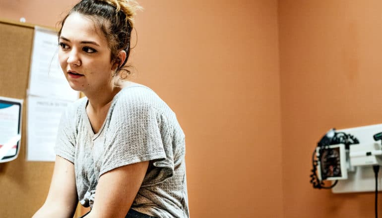 A young woman sits in an orange-painted doctor's office